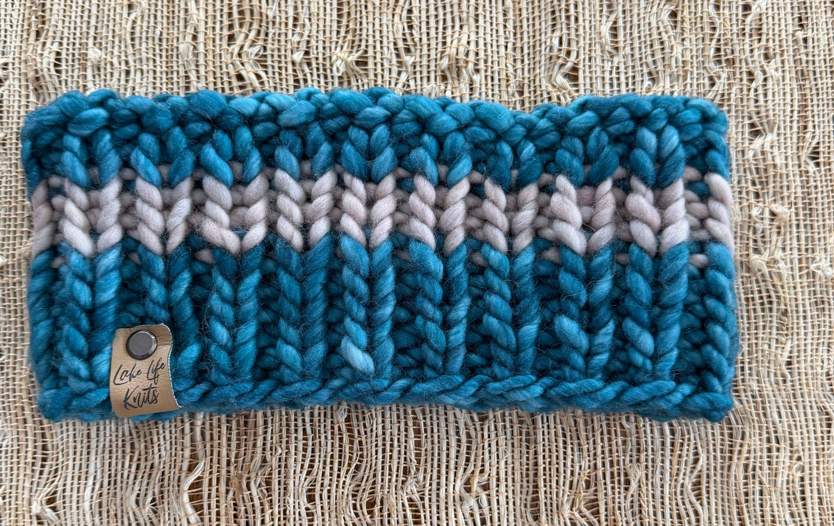 Bright turquoise chunky-knit Wildwood headband with a parchment stripe and Lake Life Knits tag, laid flat on burlap.